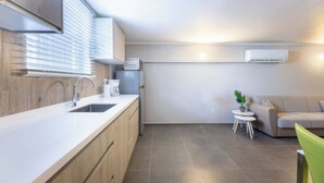 Une cuisine moderne équipée d’un évier, de placards et d’un four encastré. On y trouve une petite table ronde avec une plante, ainsi qu’un canapé dans l’espace salon.
