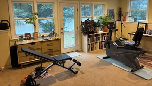 A home gym with exercise equipment, a bookshelf, and large windows. - Spacious 5-bedroom house in serene Montclair, close to NYC and World Cup arena (Montclair)