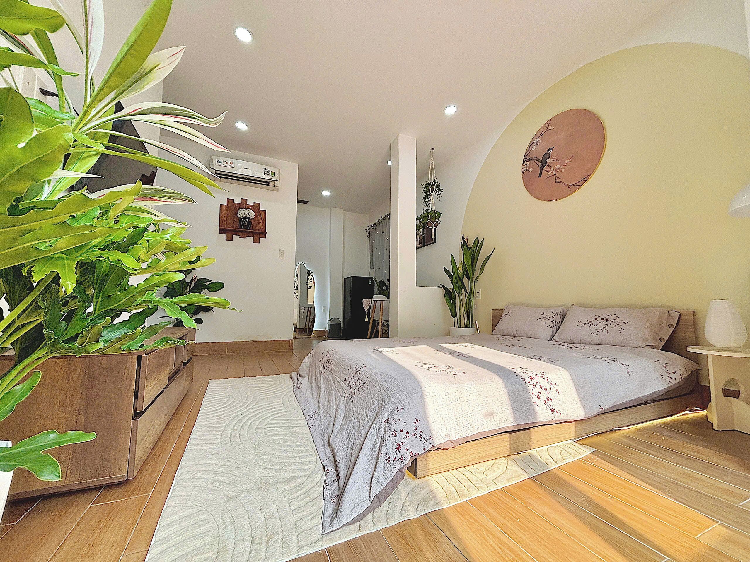 A bedroom with a bed, a large potted plant, a wall clock, and an air conditioning unit.