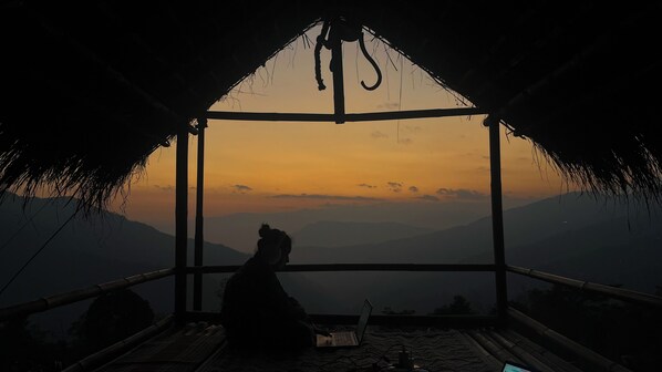 A person sitting on a bed in a room with a view of mountains at sunset. - Terra Mist by Terra Stays (Kalimpong)