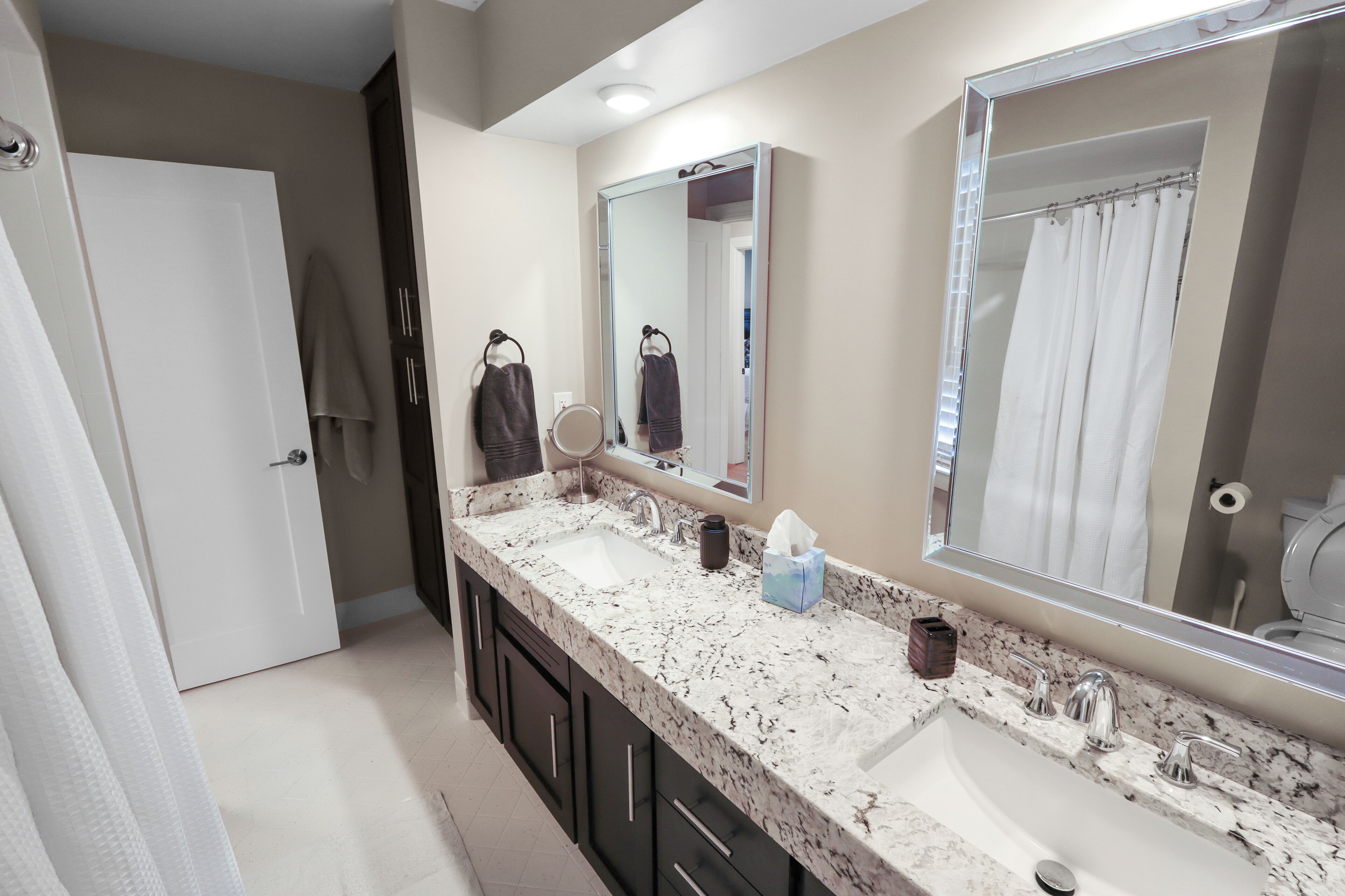 A bathroom with a double sink, two mirrors, a towel rack, and a shower curtain.