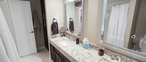 A bathroom with a double sink, two mirrors, a towel rack, and a shower curtain.
