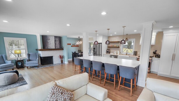 Uma sala de estar moderna com sofá, lareira e área de cozinha com banquetas e geladeira.