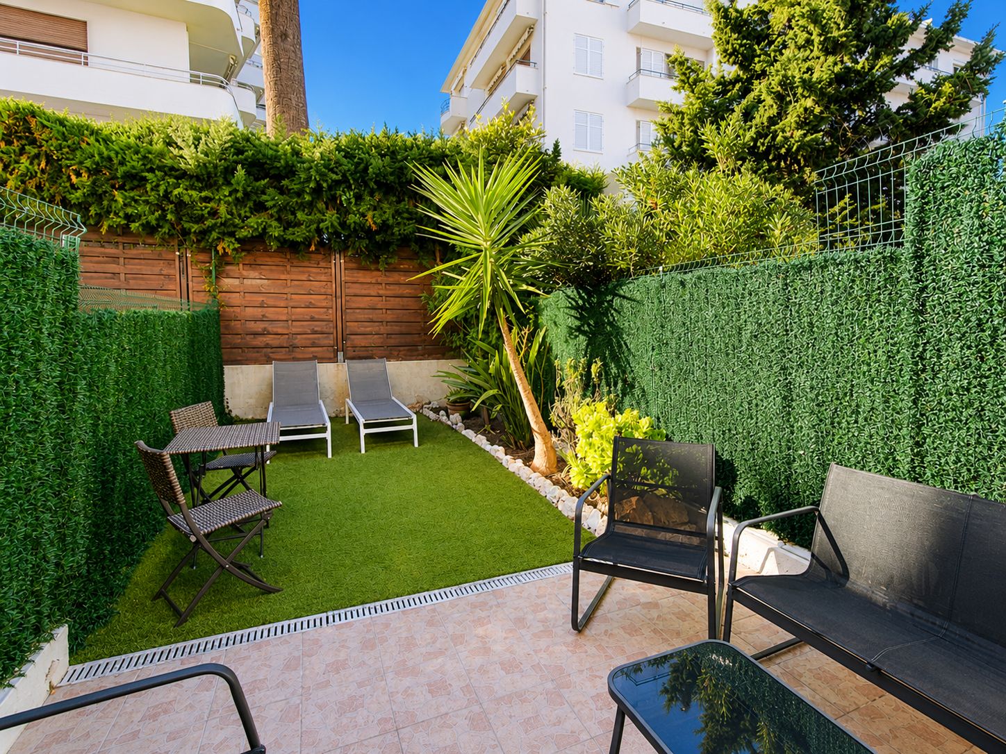 A patio with a small lawn, two lounge chairs, a table, and a sofa.