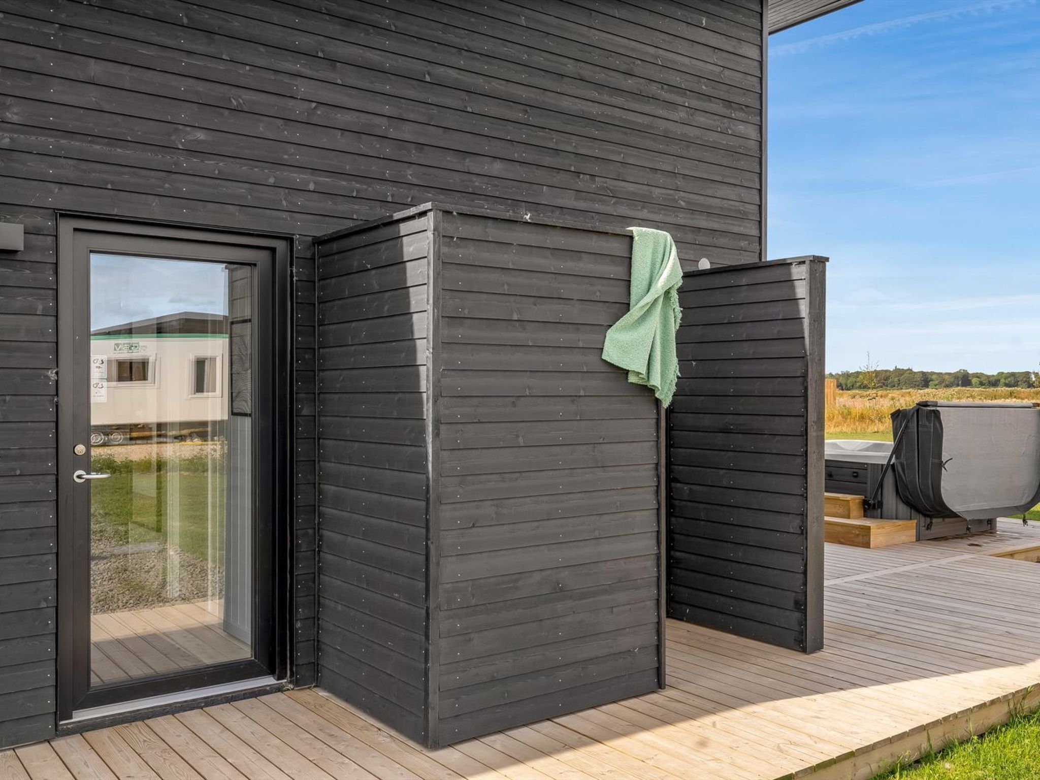 Eine moderne Sauna im Freien mit Glastür, einer Holzterrasse und Blick auf die umliegende Landschaft.
