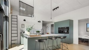 Een moderne keuken met een centraal kookeiland, barkrukken, een hanglamp en een trap.