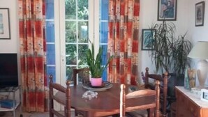Een eethoek met een houten tafel en stoelen, een potplant en een televisie op de achtergrond.