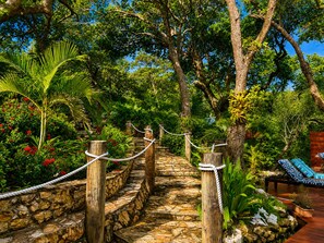 A stone pathway leading through a lush garden with wooden posts and ropes, surrounded by various tropical plants and trees. - Dancing Oaks 3BR Tropical Retreat · Saltwater Pool · Private Dock (Punta Blanca)