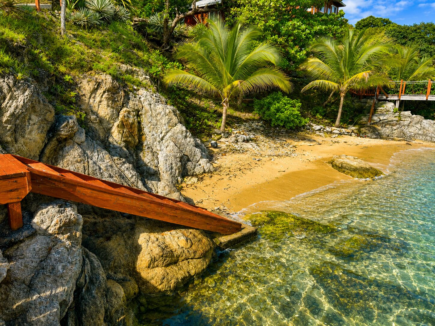 A beach with clear water, rocky shore, and palm trees.