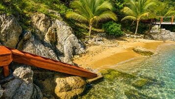 A beach with clear water, rocky shore, and palm trees.