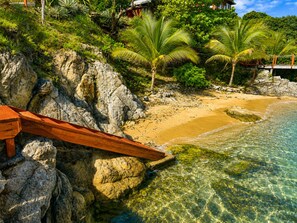 A beach with clear water, rocky shore, and palm trees.