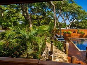 A wooden deck with a pool, surrounded by lush greenery and trees. - Dancing Oaks 3BR Tropical Retreat · Saltwater Pool · Private Dock (Punta Blanca)