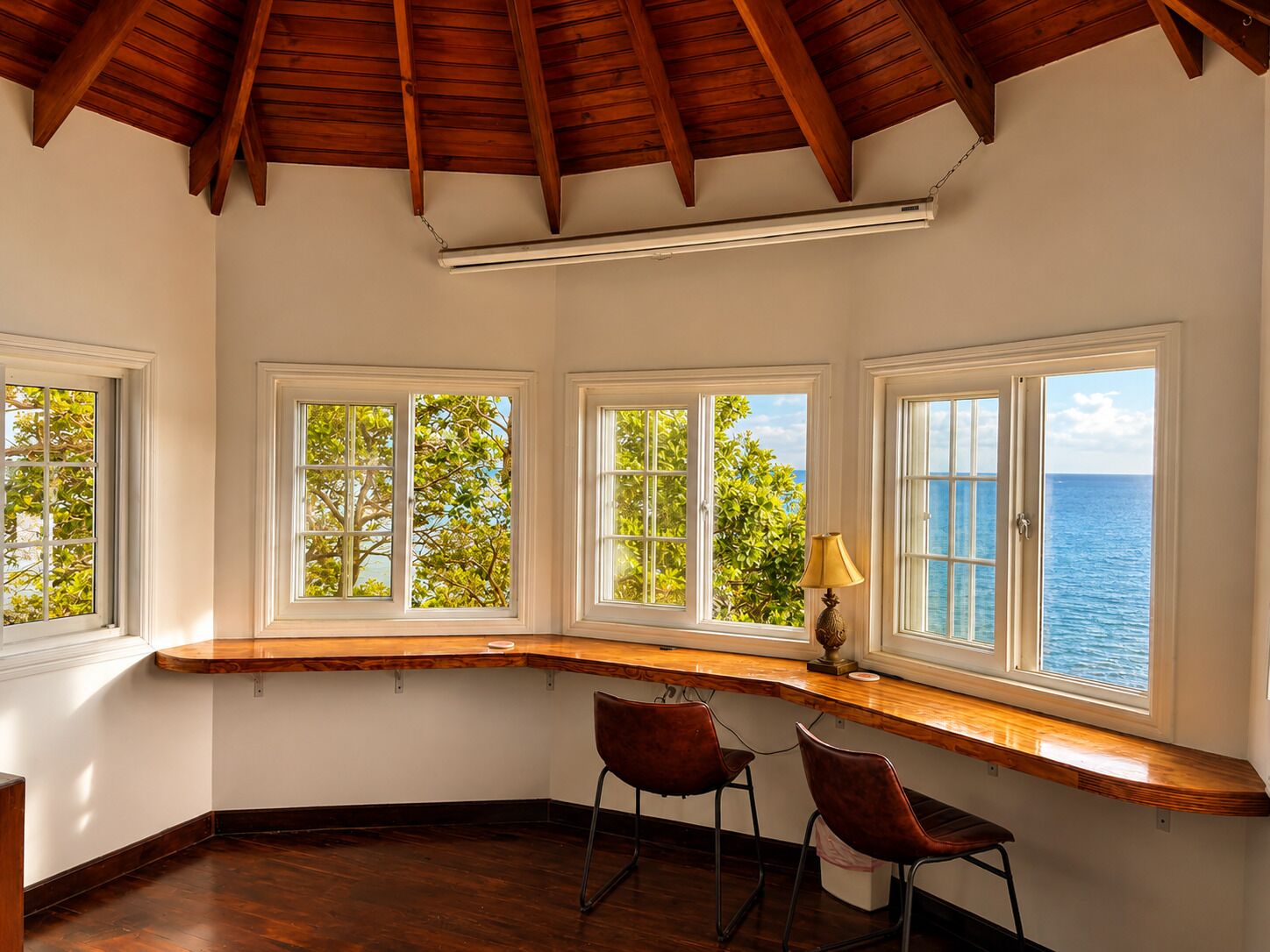 A room with a curved wooden desk, two chairs, and a view of the sea through large windows.