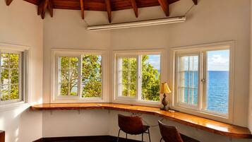 A room with a curved wooden desk, two chairs, and a view of the sea through large windows.