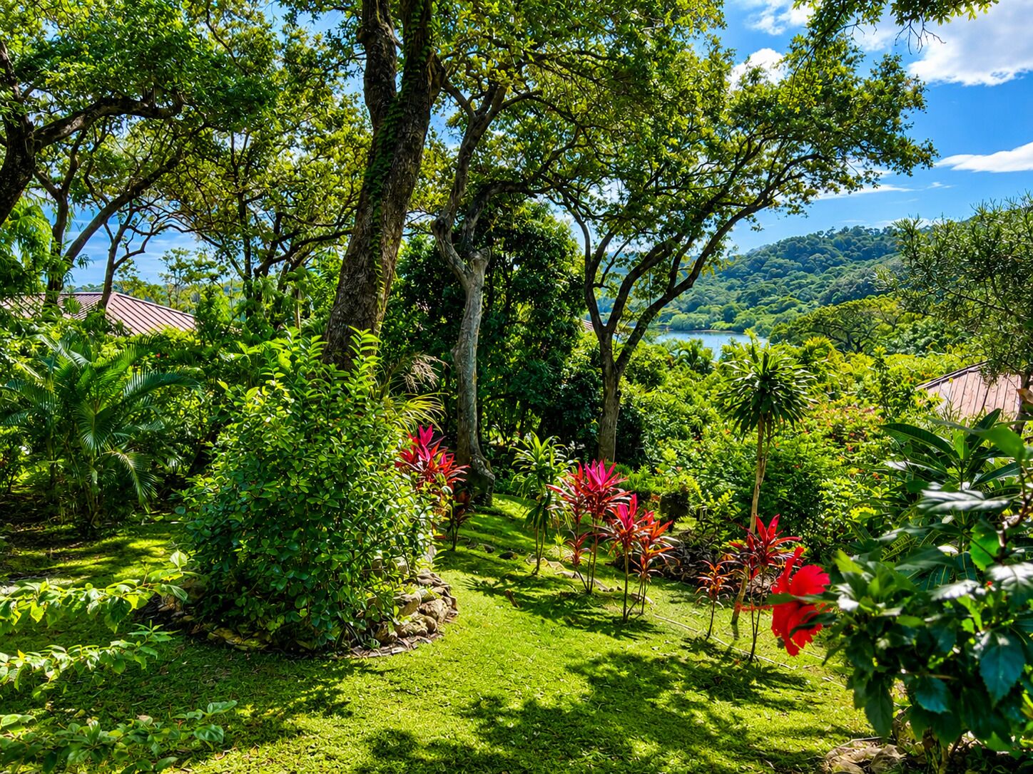A lush garden with various plants and trees, a clear sky, and a distant view of a lake and hills.