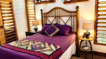 A bedroom with a wooden headboard, a bed with a purple quilt, and a nightstand with a lamp.