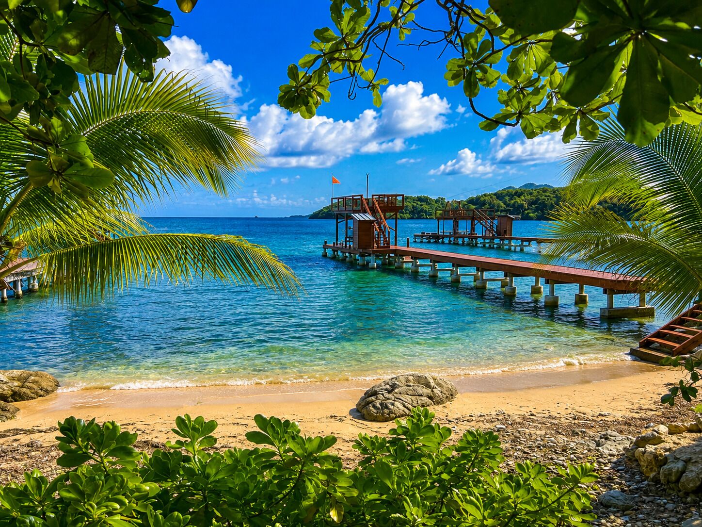 A beach with clear blue water, a wooden pier, and a small island in the background.
