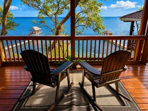 A wooden deck with two Adirondack chairs facing a view of the ocean.