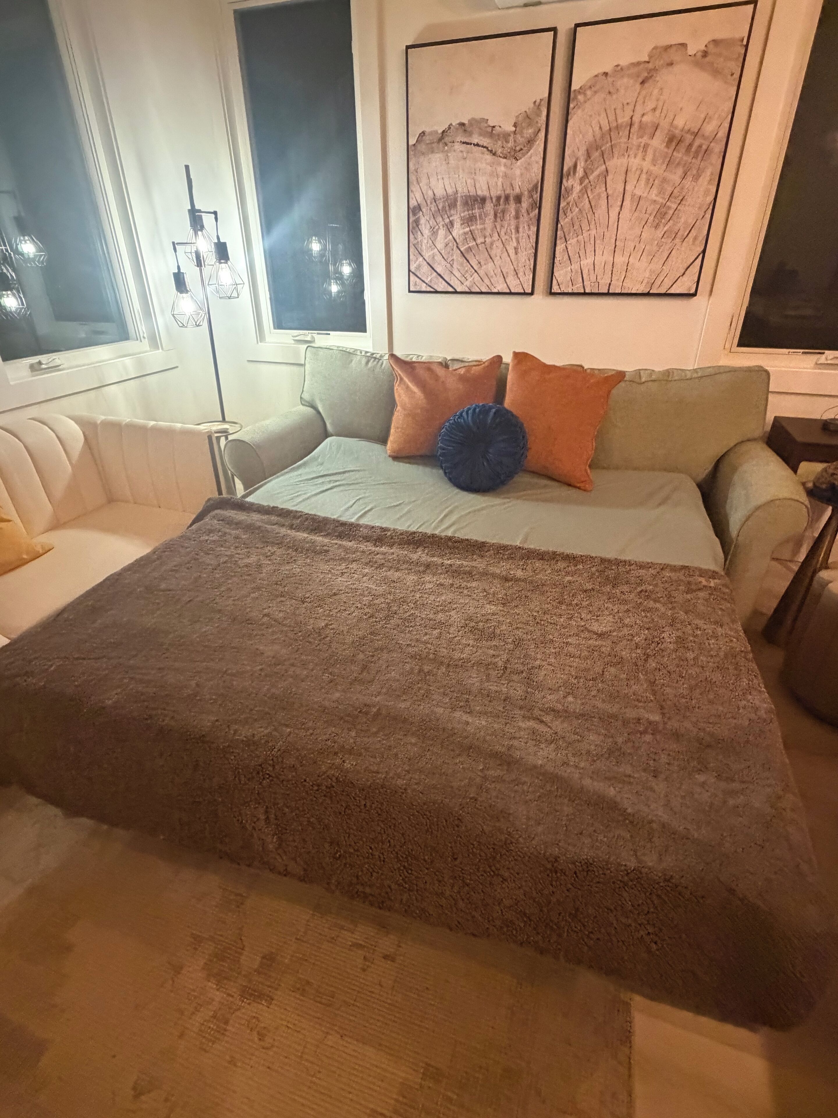 Quarto com cama, sofá, luminária de chão e parede decorada com quadros.