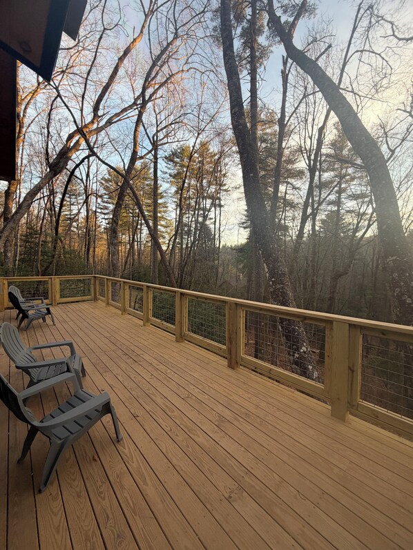 Una terraza de madera con sillas, rodeada de árboles y una barandilla de madera.
