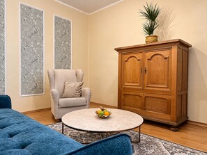A living room with a blue sofa, a round coffee table with fruit, a wooden cabinet, and a grey armchair. - 1-bedroom in Old Town (Tallinn)