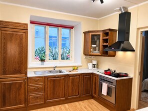 A kitchen with wooden cabinets, a window with a view, a stove, and a coffee maker. - 1-bedroom in Old Town (Tallinn)