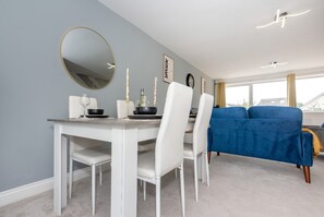 A modern dining area with a white table, chairs, and a blue sofa. - Beautiful Orpington Home w Pool Table (Orpington)