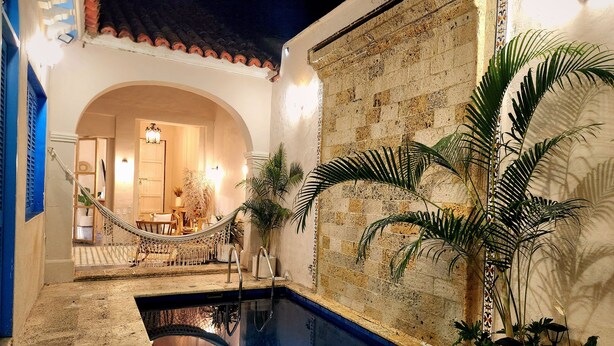 A pool area with a hammock, potted plants, and a view into a room with a chandelier. - Private house with swimming pool, jacuzzi and terrace in walled Cartagena (Cartagena de Indias)
