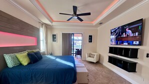 Un dormitorio con una cama grande, un ventilador de techo, un televisor montado en la pared y vistas al exterior a través de una puerta corrediza.