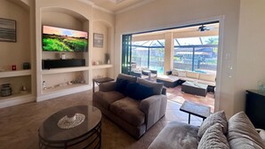 Una sala de estar con televisor, sofás, una mesa de centro y vistas a una piscina y zona exterior.