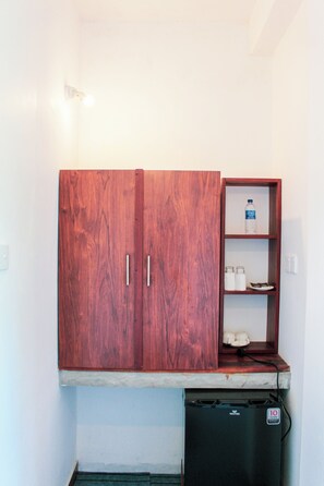 A compact kitchenette with a wooden cabinet, a small shelf with glassware, and a black dishwasher. - Velora Hill Ella (Ella)
