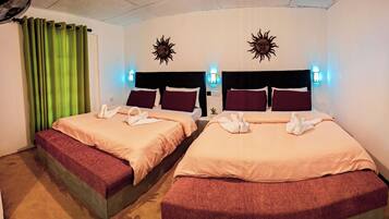 Habitación de hotel con dos camas, cortinas verdes, adornos de sol colgados en la pared y una mesita de noche pequeña con una planta.