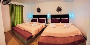 Ein Hotelzimmer mit zwei Betten, grünen Vorhängen, Wanddekorationen mit Sonnensymbolen und einem kleinen Nachttisch mit Pflanze.