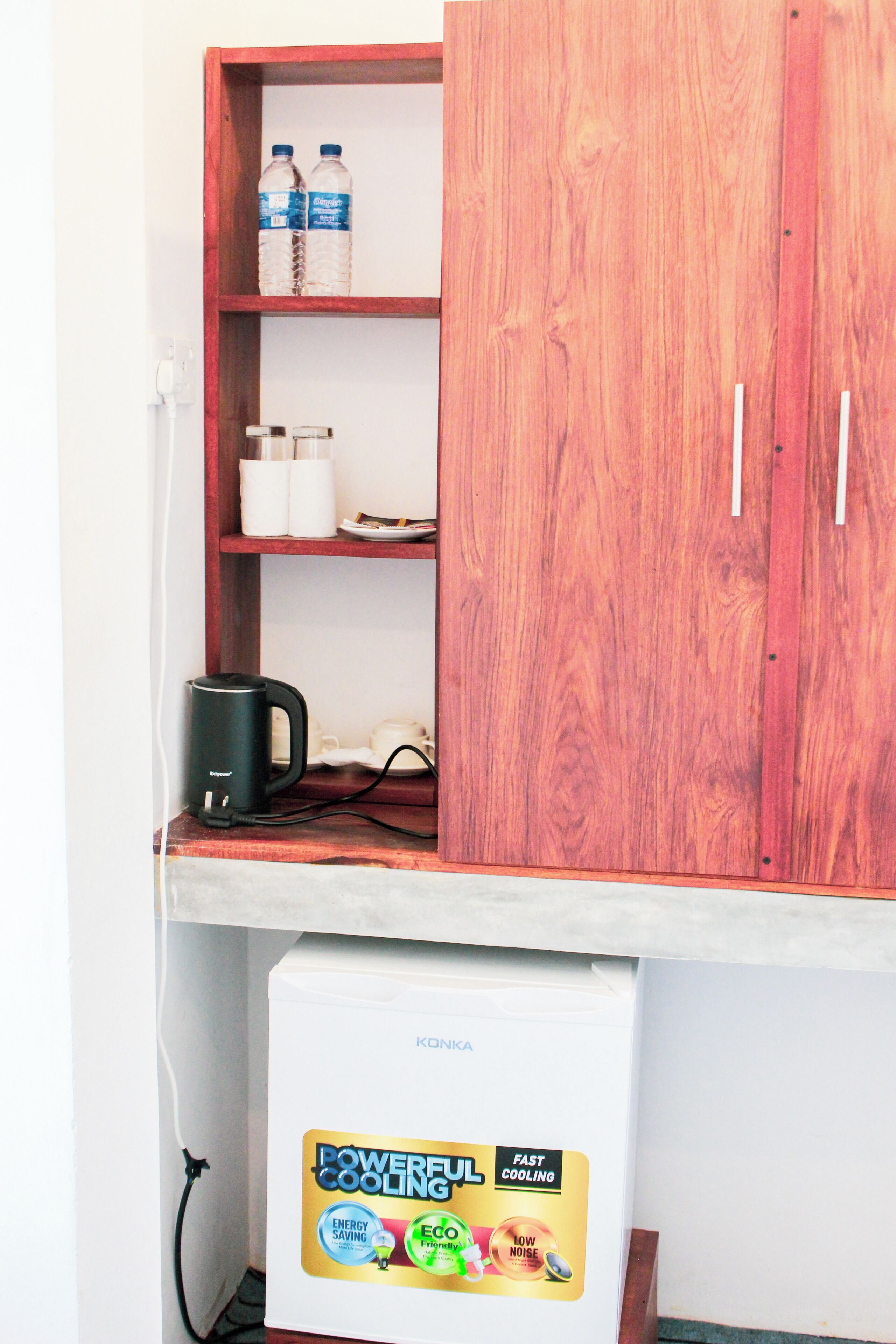A wooden cabinet with two bottles, a kettle, and a small refrigerator with a 'Powerful Cooling' label.