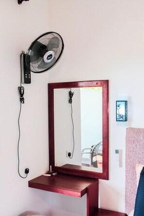 A room with a wall-mounted mirror, a standing fan, and a small wooden shelf. - Velora Hill Ella (Ella)