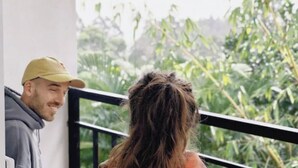 A balcony with a view of green foliage and a white building in the background. - Velora Hill Ella (Ella)