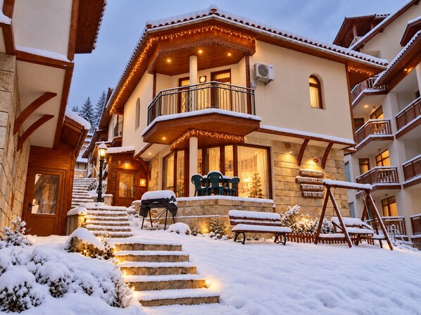 A hotel with a snow-covered exterior, a wooden staircase leading to the entrance, and outdoor seating.