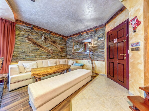Una sala de estar acogedora con una pared de piedra, un banco de madera, un sofá y una puerta roja con un cartel de 'No Smoking'.