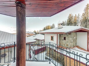 A covered balcony with a metal railing, overlooking a snowy landscape with buildings and trees. - Alpine Villas Pamporovo (Smolyan)