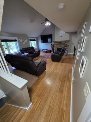 A spacious living room with a fireplace, a ceiling fan, and a large TV. - Valley Trail Riverfront Townhouse with EV Charging 2 miles from Mount Snow (Dover)