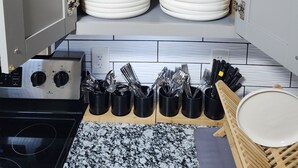 Una cocina con armarios blancos, estantes con platos y vasos apilados, una estufa y utensilios sobre la encimera.