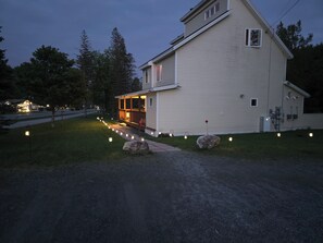 A two-story house with a porch and a pathway lit by string lights. - Valley Trail Riverfront Townhouse with EV Charging 2 miles from Mount Snow (Dover)