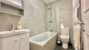 A modern bathroom with a bathtub, toilet, and a glass-enclosed shower. - Bright Apartment Stockwell Station Nearby (London)