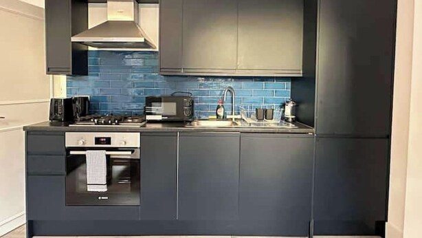 A compact kitchen with dark cabinetry, a built-in oven, and a microwave. - Bright Apartment Stockwell Station Nearby (London)
