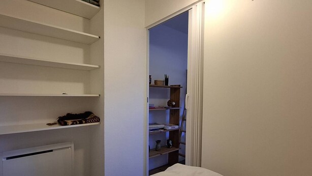 A bedroom with a bed, a closet with shelves, and a door leading to another room. - Renovated studio cabin near slopes, 4 pers. (Bolquère-Pyrénées 2000)