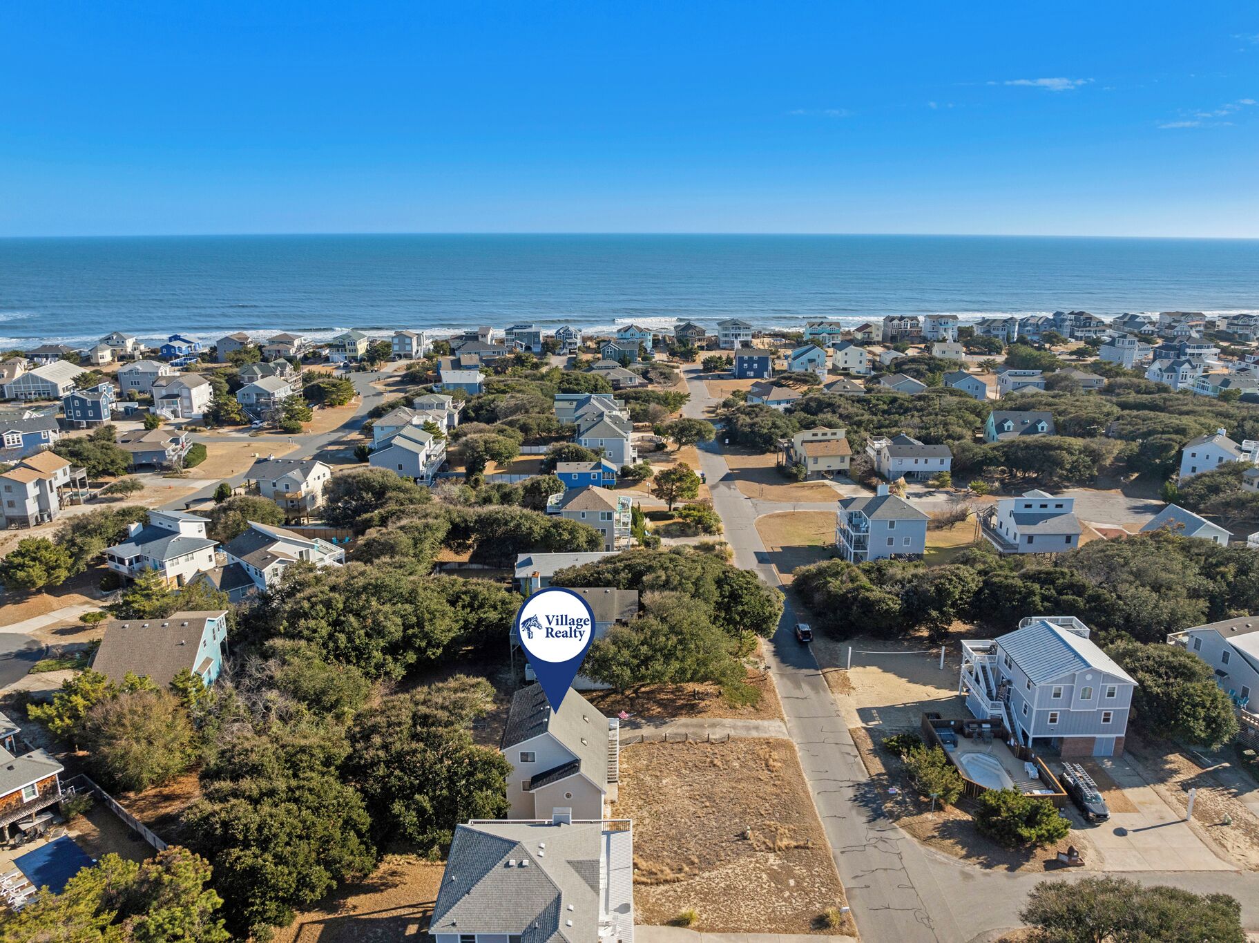 An aerial view of a coastal residential area with houses, a clear blue sky, and the ocean in the background.