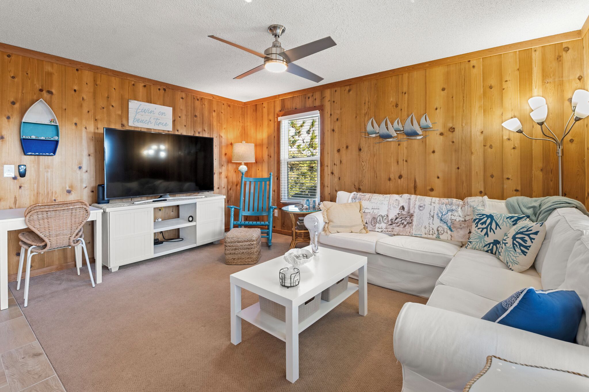 Ein Wohnzimmer mit Fernseher, weißem Sofa und Deckenventilator.