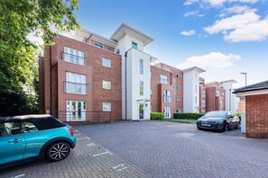 A modern apartment complex with brick and white exterior walls, a paved driveway, and parked cars. - Quiet Ground-Floor Apartment | Heathrow, Windsor & London at Your Doorstep (Slough)