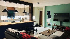A modern living room with a sofa, a coffee table, and a TV. There's a kitchen area with a microwave and a sink. - Beautiful Lakefront house with private dock, boathouse, Hot tub and Game-room (Sebring)