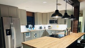 A modern kitchen with a stainless steel refrigerator, a wooden countertop, and hanging pendant lights. - Beautiful Lakefront house with private dock, boathouse, Hot tub and Game-room (Sebring)